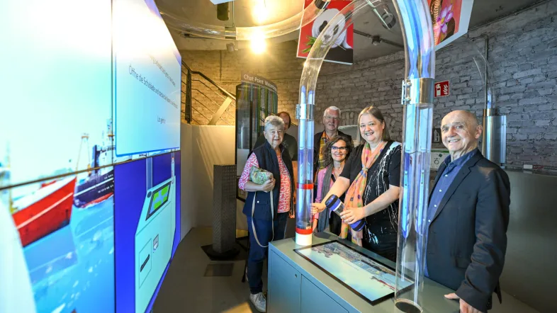 Gruppe bei einer Führungsrunde im Aquarius Wassermuseum Mülheim, geführt von einer Museumsperson vor multimedialer Ausstellung.