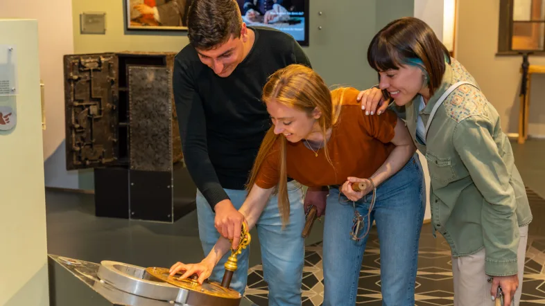Ein Mann und zwei Frauen versuchen, ein Trickschloss in der Dauerausstellung zu öffnen.