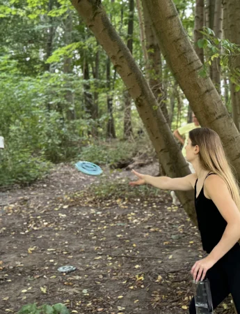Frau wirft Frisbee beim Disc Golf im Wald in Dortmund.