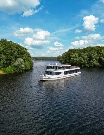 Foto eines Fahrgastschiffes mit zwei Decks, auf denen viele Touristen die Rundfahrt auf dem Halterner Stausee genießen. Links und rechts neben dem Schiff sind grün bewachsene Inseln zu sehen und die Schneise, durch die das Schiff durchgefahren ist. Der Himmel ist blau und mit einigen weißen Wolken durchzogen, das Wasser spiegelt leicht den Himmel und das Schiff wider.