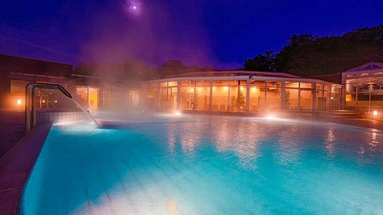 Außenbad im Revierpark Nienhausen bei Nacht, beleuchtet von sanften Lichtern und umgeben von dunkler Natur.