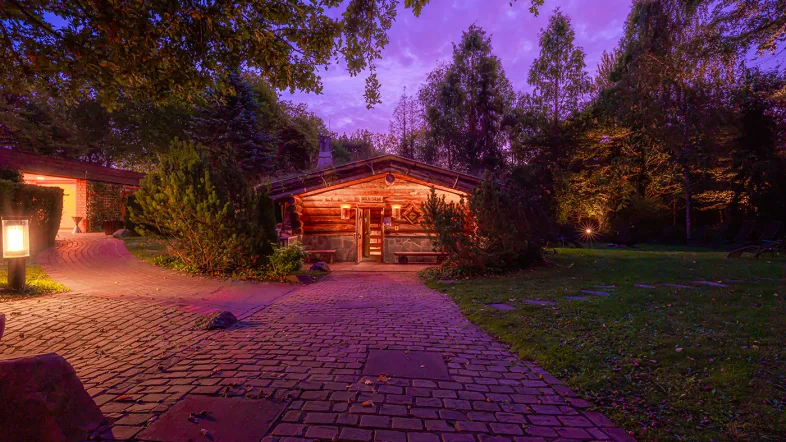 Gehweg im Revierpark Nienhausen führt ruhig und schattig zur Sauna, umgeben von grünen Bäumen.