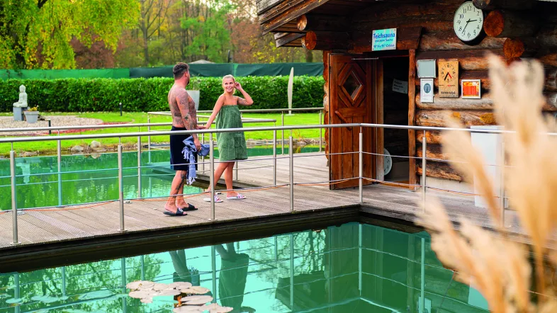 Paar geht gemeinsam den Weg zur Sauna im Revierpark Vonderort entlang, umgeben von grüner Natur.