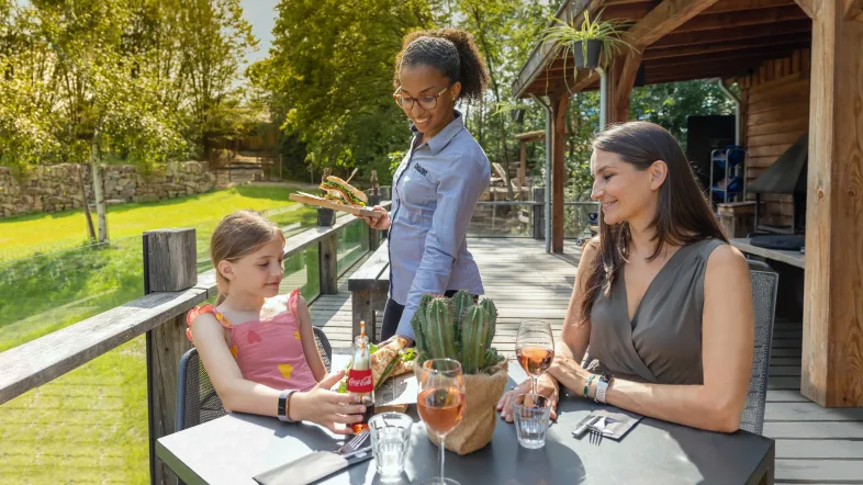 GaiaZoo Mutter mit Kind sitzen an einem Tisch und bekommen von einer Kellnerin das Essen serviert