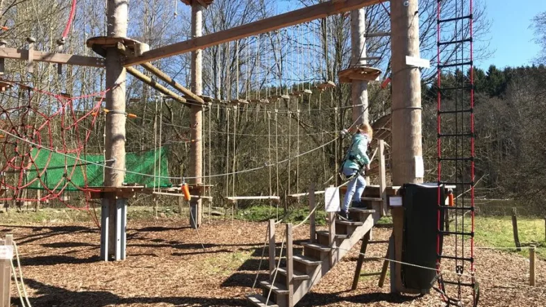 Kind mit Kletterausrüstung balanciert auf einem Parcours im Kletterpark Biggesee.