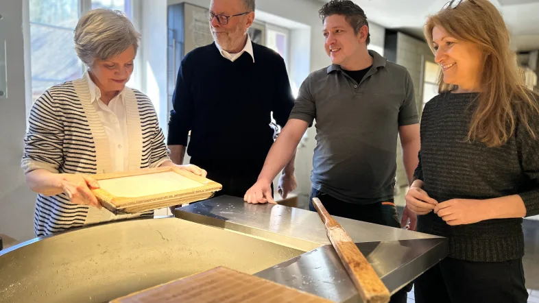 4 Menschen stehen um einen Tisch und erhalten eine Erklärung zu Papier