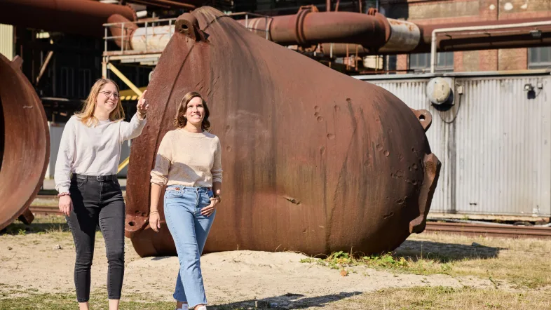 Zwei Besucherinnen vor rostigen Pfannen, in denen früher das Roheisen transportiert wurde.