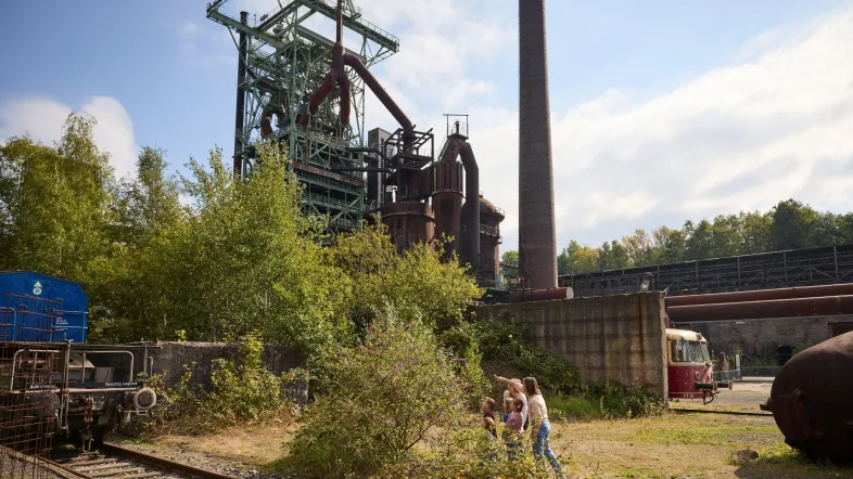 Hochofen der Henrichshütte mit grünen Sträuchern und einer kleinen Besuchergruppe im Vordergrund:
