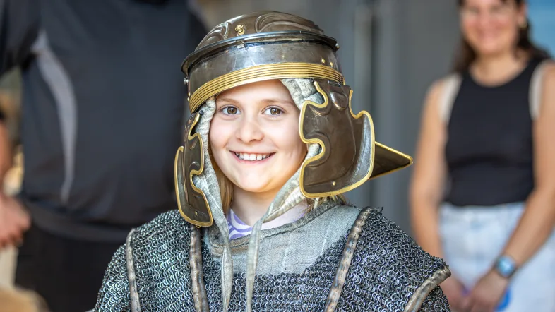 Ein Kind probiert im Museum eine römische Rüstung an.