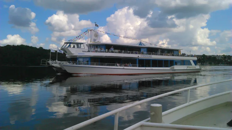 Seitenansicht eines Fahrgastschiffs auf dem Möhnesee bei ruhiger Wasseroberfläche und blauem Himmel.
