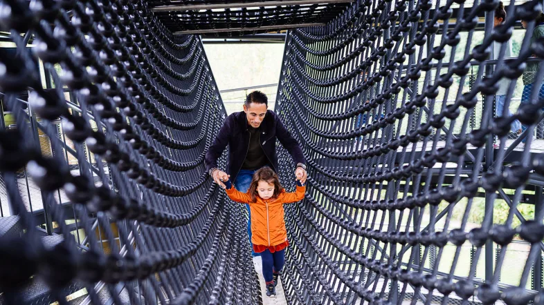 Ein Vater läuft mit seiner Tochter durch den Klettertunnel auf dem Erlebnisturm Höhlenblick