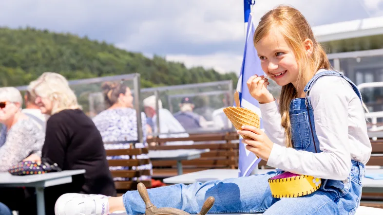 Mädchen genießt Eis auf einem Ausflugsboot während der Schifffahrt auf dem Biggesee an einem sonnigen Tag.