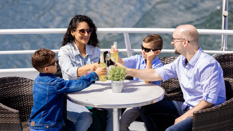 Familie stößt fröhlich mit Getränken auf einem Ausflugsboot während einer Schifffahrt auf dem Biggesee an.