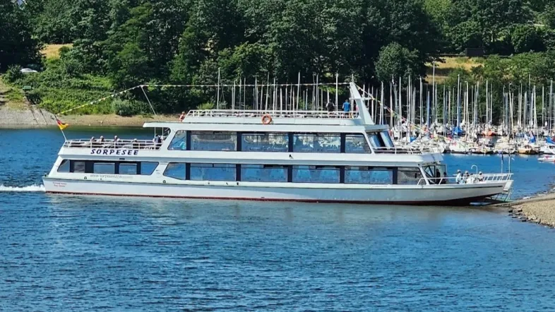 Seitenansicht eines Fahrgastschiffs auf dem Sorpesee, vor bewaldetem Ufer und klarem Himmel.