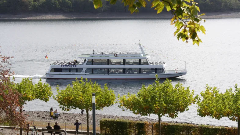 Ausflugsschiff auf dem Sorpesee, aufgenommen aus der Ferne mit sichtbarer Wasserfläche und bewaldeten Ufern.