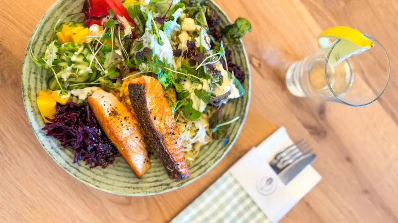 Ein Teller mit Salat und Fisch, Besteck und Tafelwasser im Glas mit Zitrone