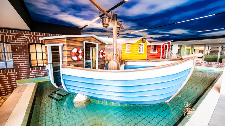 großer blauer Kahn mit brauner Holzkabine und weitere Spielhütten im Kinderbecken zum spielen und begehen