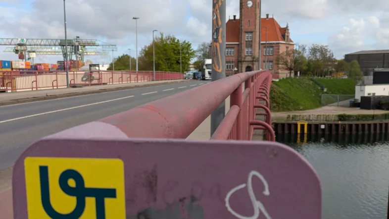 Foto von einer Brücke über einem Fluss mit dem Urban.Trails Aufkleber.