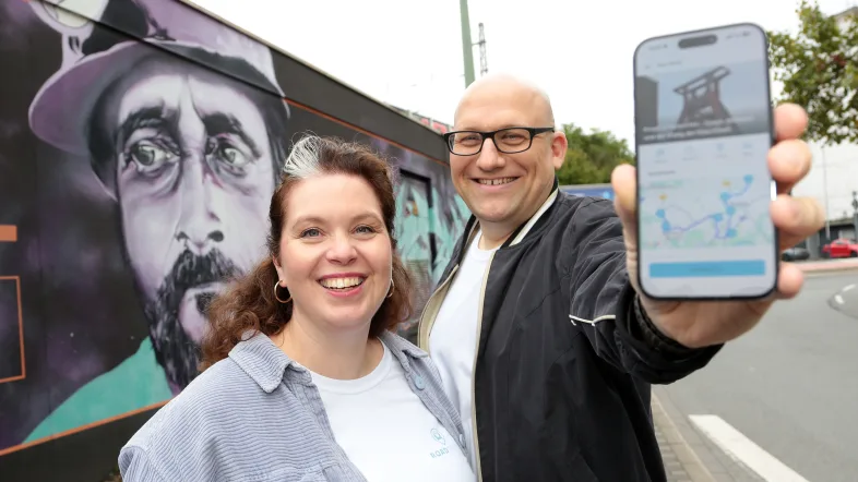 Zwei Personen halten ein Handy mit der geöffneten Roadstory App in die Kamera.