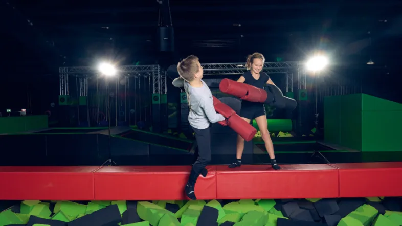 Zwei Kinder spielen mit Battle Sticks vor einem Foam Pit