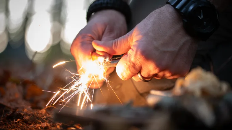 Hände die mithilfe von Stock und Stein ein Feuer zünden