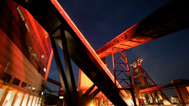 Zeche Zollverein Essen bei Abenddämmerung mit stimmungsvoll beleuchteten Industrieanlagen.