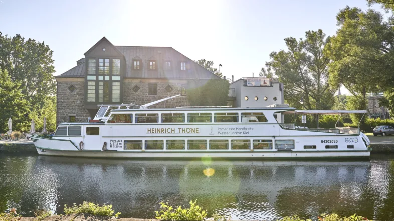 Seitenansicht des Ausflugsschiffs „Weiße Flotte“ auf dem Fluss in Mülheim bei klarem Himmel.