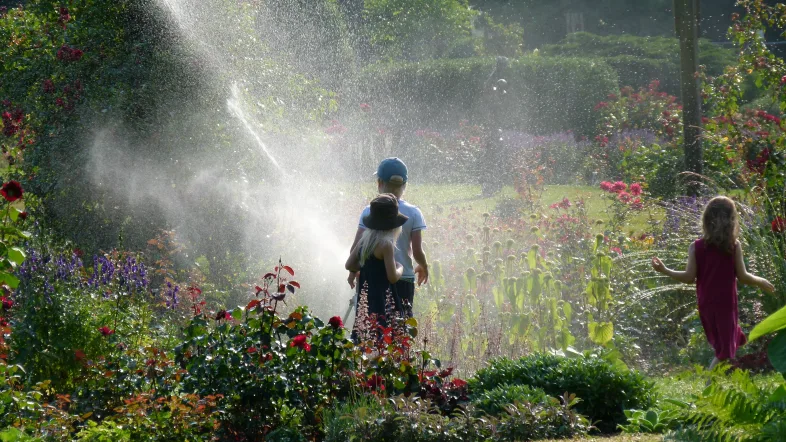 Kinder stehen spielend im Wassersprenkler des Westfalenparks Dortmund an einem warmen Sommertag.