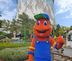 Maskottchen mit blauer Latzhose vor einem Fahrgeschäft